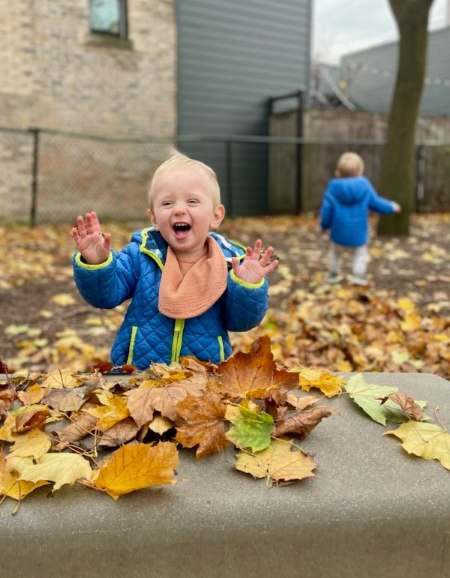 A different little boy playing in fallen leaves