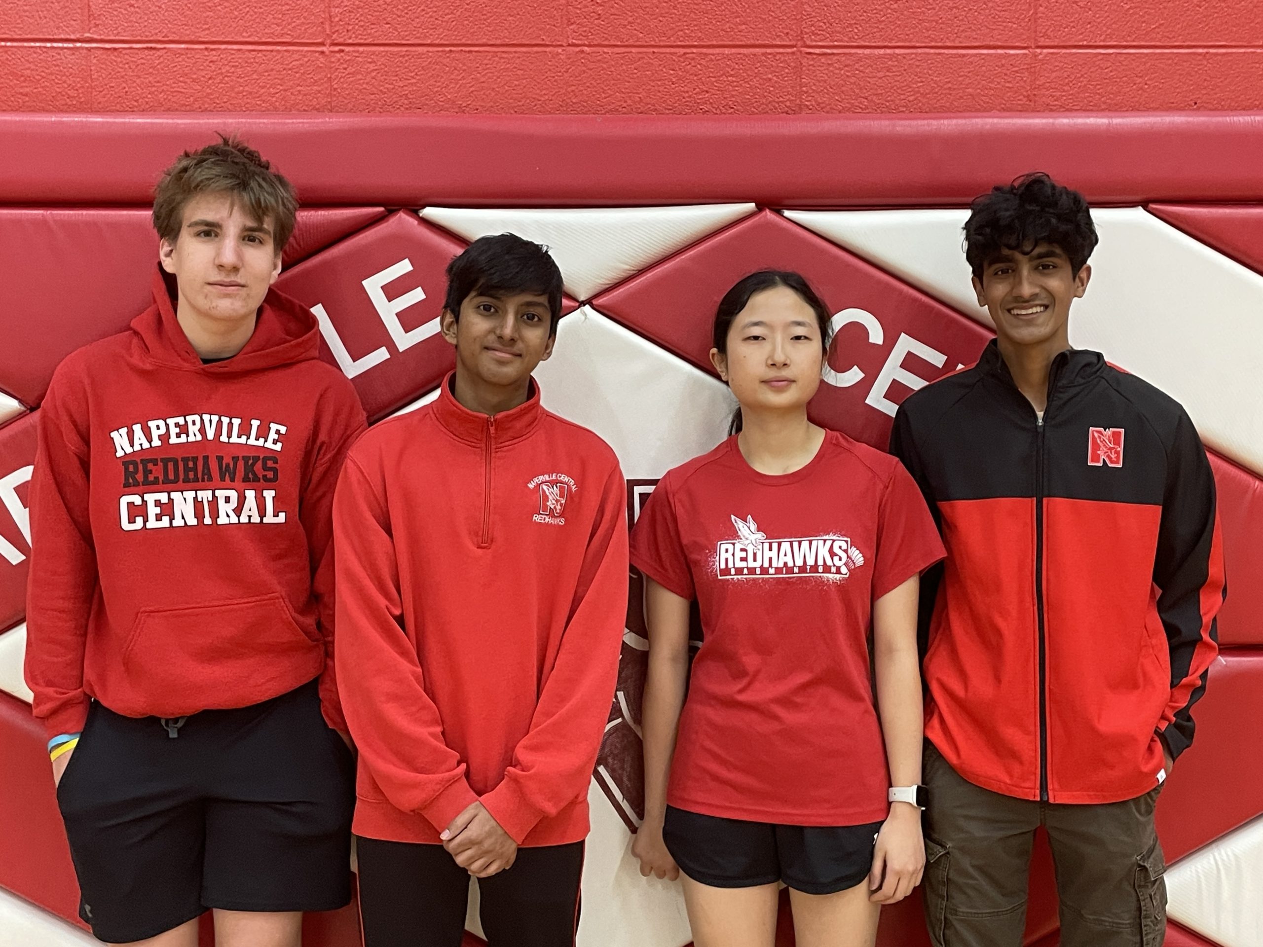 Four high school students, three young men and one young woman, smiling and standing against a red and white background