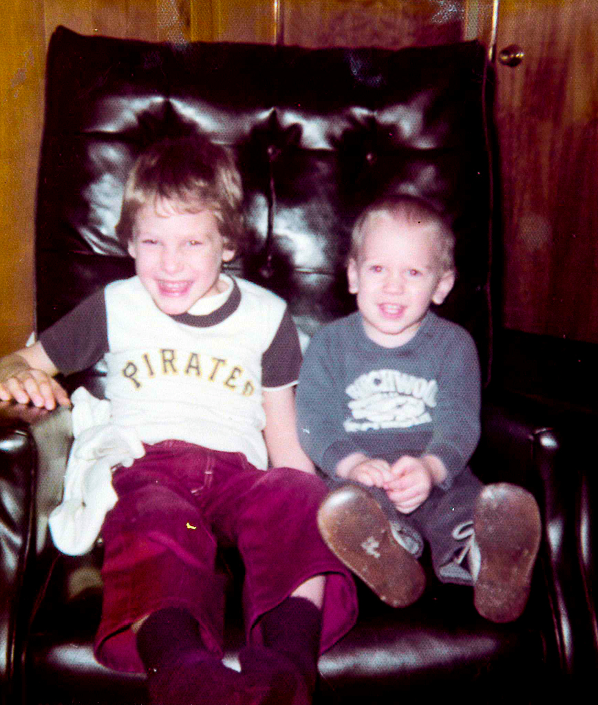 Two young boys, around ages six and four, sitting in an easy chair and smiling